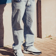 Person wearing a patterned jacket, jeans, and white sneakers against a blue wall.